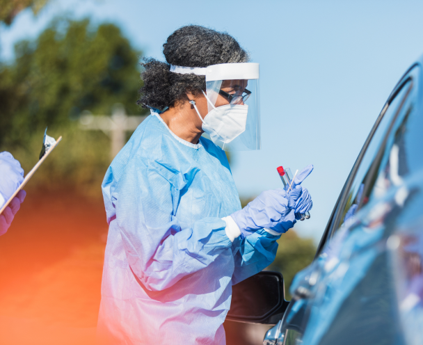 Equipped healthcare worker speaking with someone inside a car